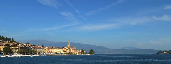 Familienurlaub beliebte Urlaubsziele am Gardasee -  Mit einer Fläche von 370 km² ist der Gardasee der größte See Italiens. Es liegt am Fuße der Alpen und erstreckt sich über drei Staaten: Lombardei, Venetien und Trentino. Die maximale Tiefe des Sees beträgt 346 m, er hat eine längliche Form und sein nördliches Ende ist sehr schmal. Dort ist der See von den Bergen der Gruppo di Baldo umgeben. Du trittst aus deinem gemütlichen Hotelzimmer und es begrüßt dich die warme italienische Sonne. Du blickst auf den atemberaubenden Gardasee, der in zahlreichen Blautönen schimmert - von tiefem Dunkelblau bis zu funkelndem Türkis. Majestätische Berge umgeben dich, während die Brise sanft deine Haut streichelt und der Duft von blühenden Zitronenbäumen deine Nase kitzelt. Du schlenderst die malerischen, engen Gassen entlang, vorbei an farbenfrohen, blumengeschmückten Häusern. Vereinzelt unterbricht das fröhliche Lachen der Einheimischen die friedvolle Stille. Du fühlst dich wie in einem Traum, der nicht enden will. Jeder Schritt führt dich zu neuen Entdeckungen und Abenteuern. Du probierst die köstliche italienische Küche mit ihren frischen Zutaten und verführerischen Aromen. Die Sonne geht langsam unter und taucht den Himmel in ein leuchtendes Orange-rot - ein spektakulärer Anblick.